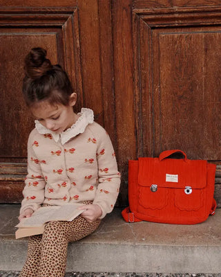 Cardigan beige à motif jacquard rouge pour enfant, en maille douce avec fermeture boutonnée.