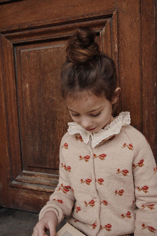 Cardigan beige à motif jacquard rouge pour enfant, en maille douce avec fermeture boutonnée.